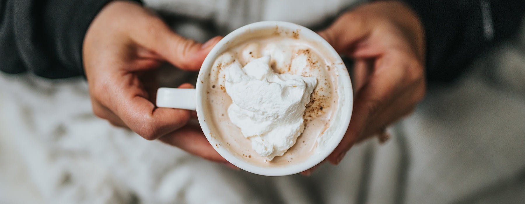 overhead shot of hands holding a mug of hot chocolate with whipped cream